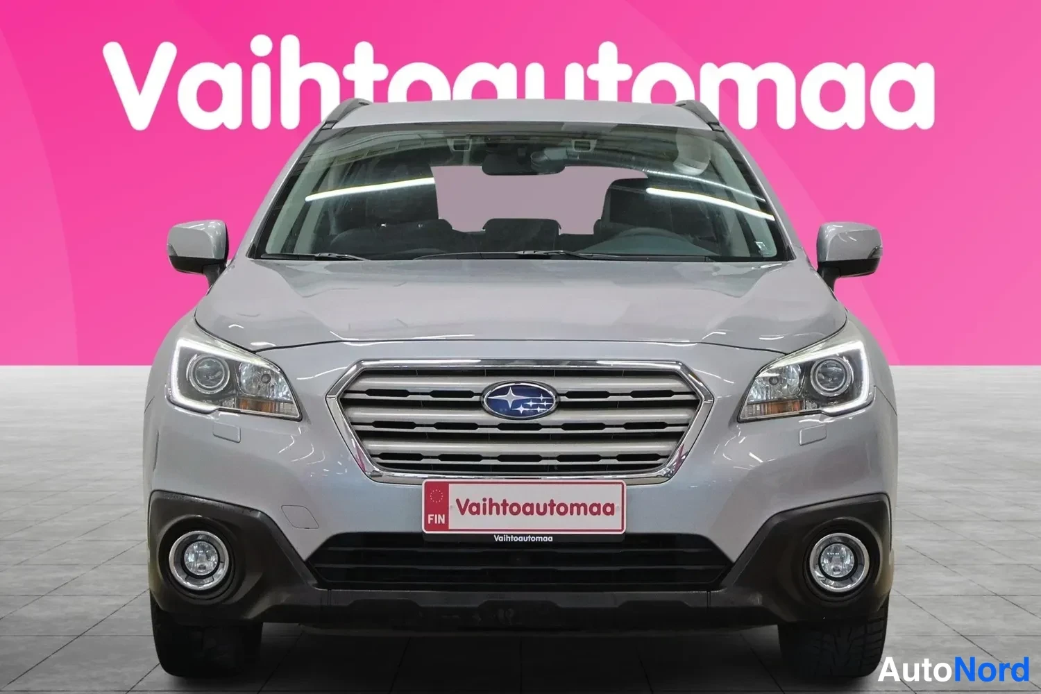 Edestä: Front-on view of a silver Subaru Outback against a pink background with 'Vaihtoautoamaa' text overlay.
