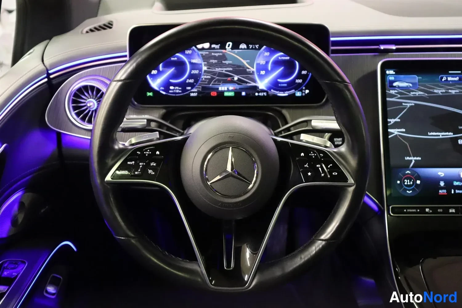 Muu: Ohjauspyörän lähikuva Mercedes-ohjaamossa, taustalla digitaalinen mittaristo ja karttanäyttö.