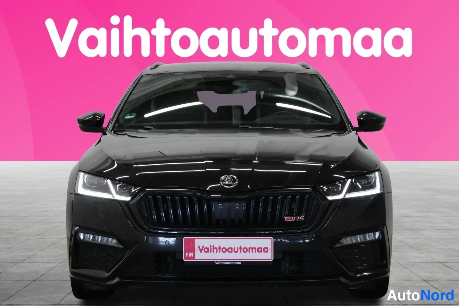 Edestä: Musta Skoda Octavia vakioliikennevaloissa eteenpäin katsovana. Vasen suuntalaita on valottamassa.