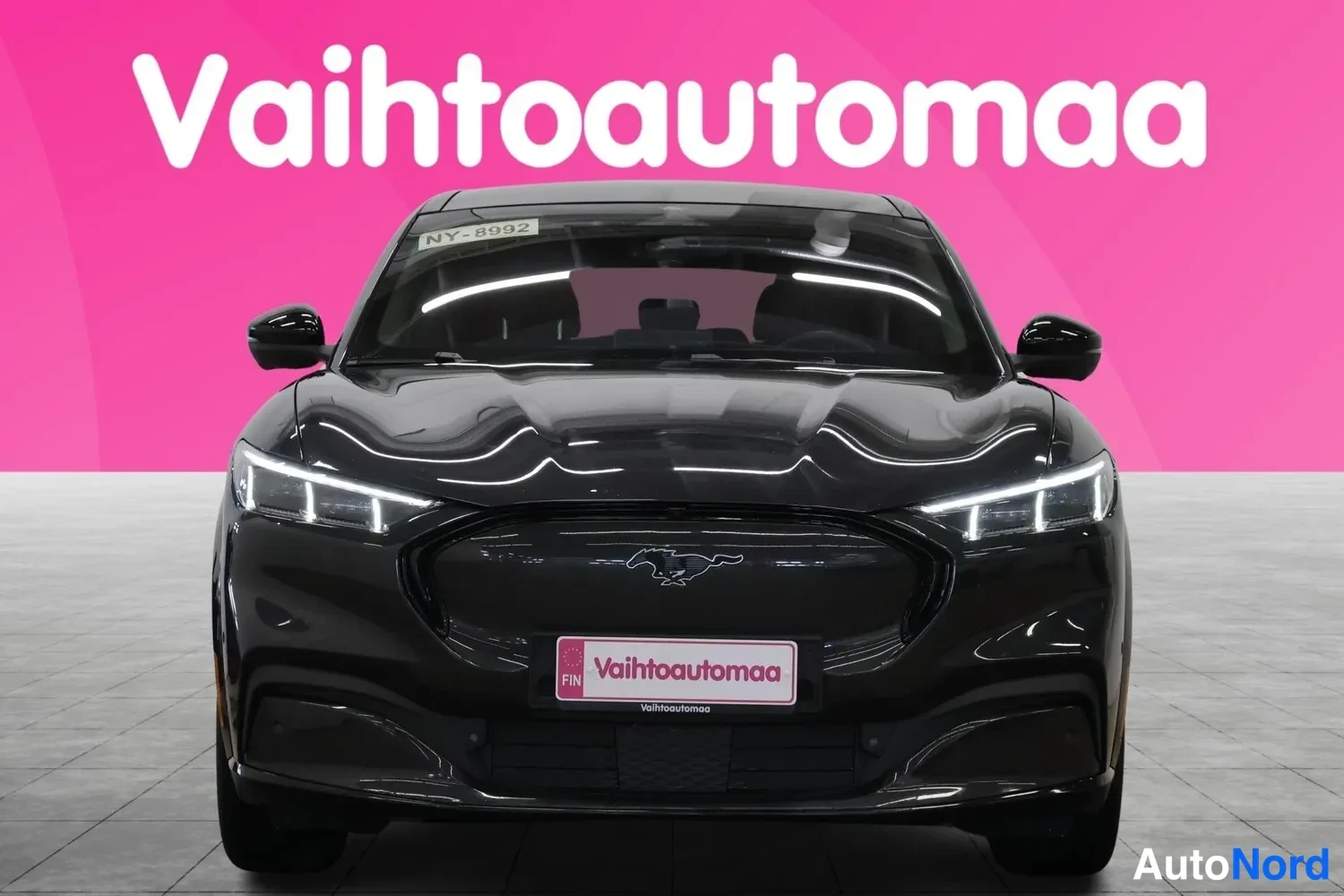Edestä: Musta Ford Mustang Mach-E suoraan edestä kuvattuna, etusäleikkö ja LED-ajovalot näkyvissä.