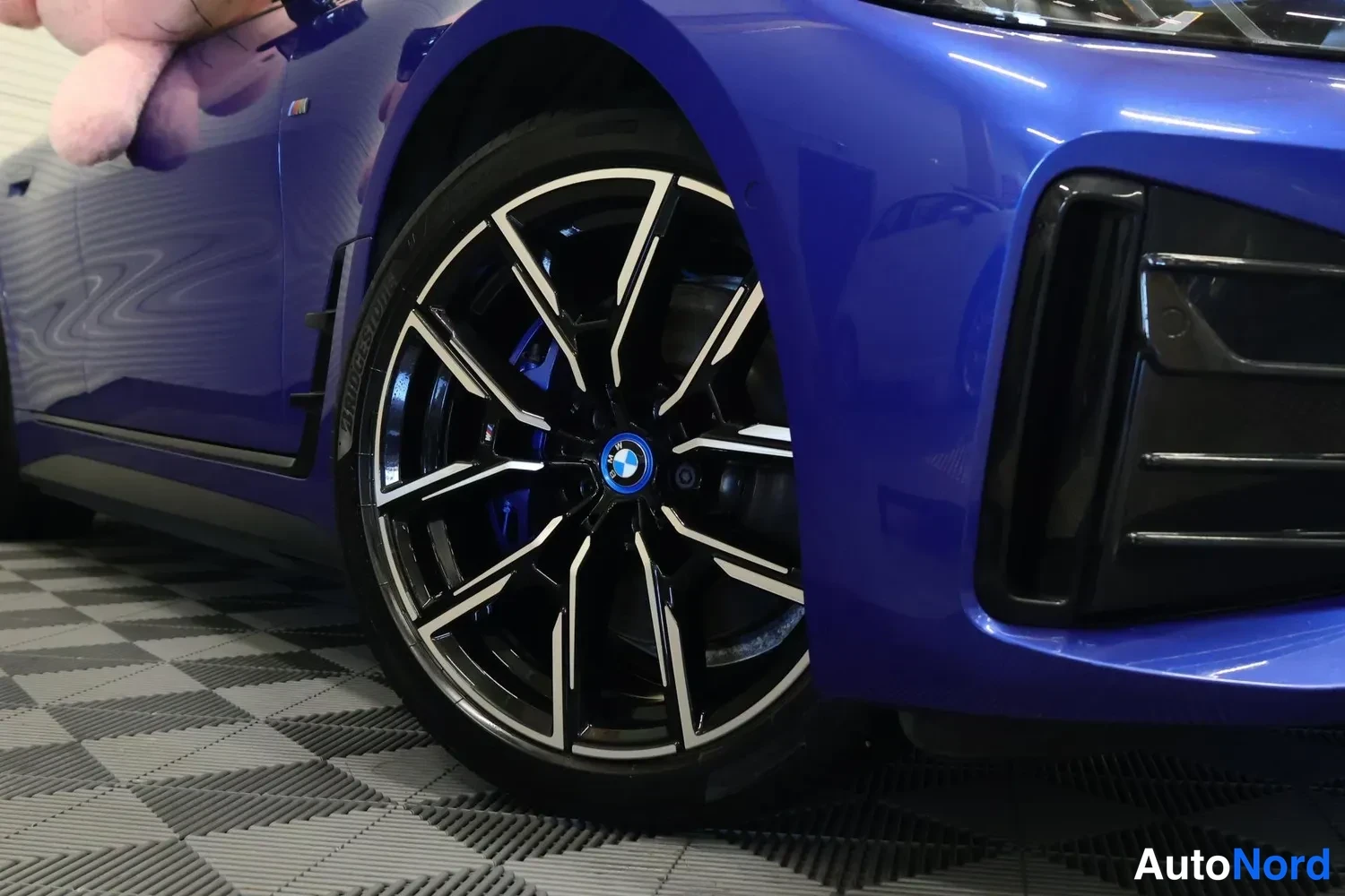 Etuviisto, nokka oikealle: Lähikuva etupyörästä: tumma BMW-vante, sininen jarrusatula, sininen kori ja etupuskurin musta ilmanotto.