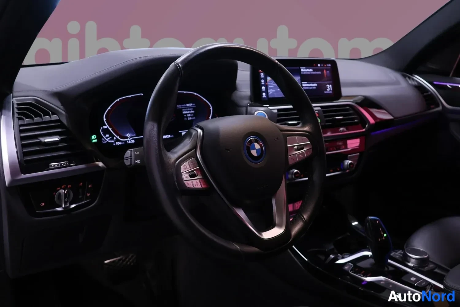 Yksityiskohta: Ohjaamo sivulta: BMW-ratti, digitaalinen mittaristo, keskikonsolin näyttö ja automaattivaihteen valitsin.