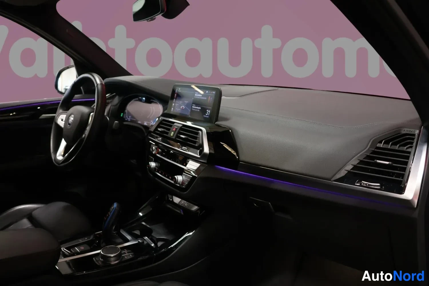 Edestä: Näyttö kuvaa BMW iX3:n etuosaa sisätilassa: vanteen, ohjauspyörän ja infotainment-näytön ympäristö.