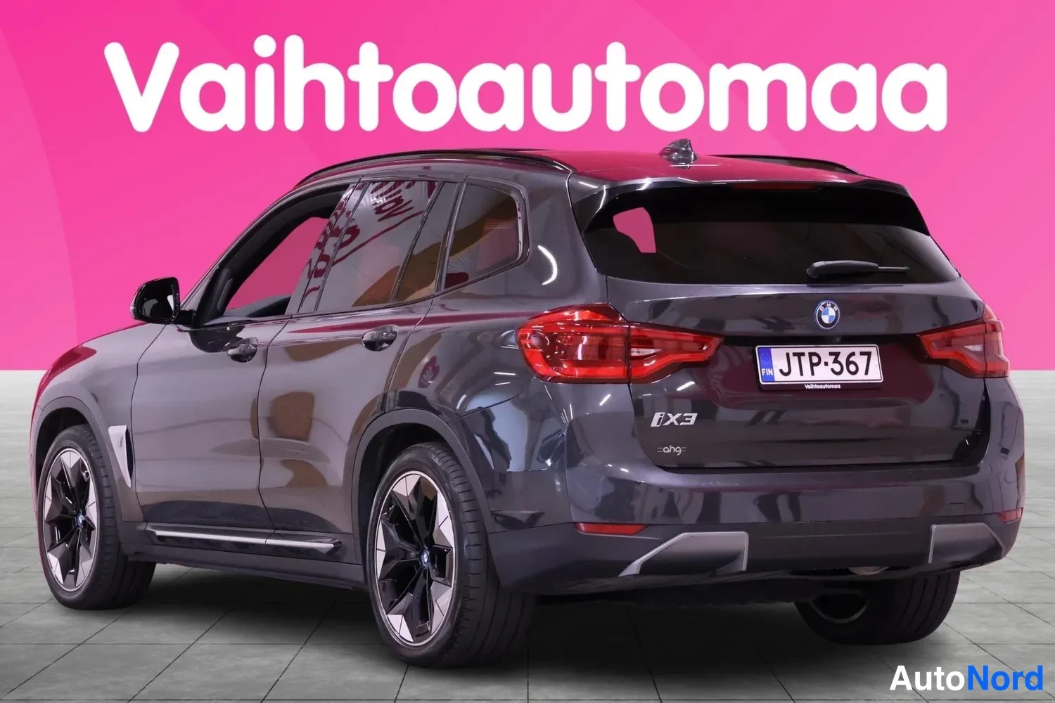 Takaviisto: Auton takanurkkaus: takapää ja vasen sivu näkyvissä, rekisteri, vaaleanharmaa lattia, vaaleanpunainen tausta tekstillä Vaihtoautomaa.