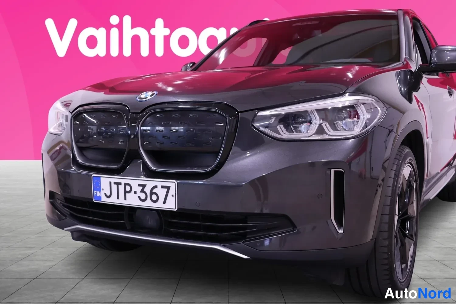 Etuviisto, nokka vasemmalle: Lähikuva auton etupäästä: musta BMW-etusäleikkö, headlights, rekisteri, oikean etupyörän reuna näkyvissä.