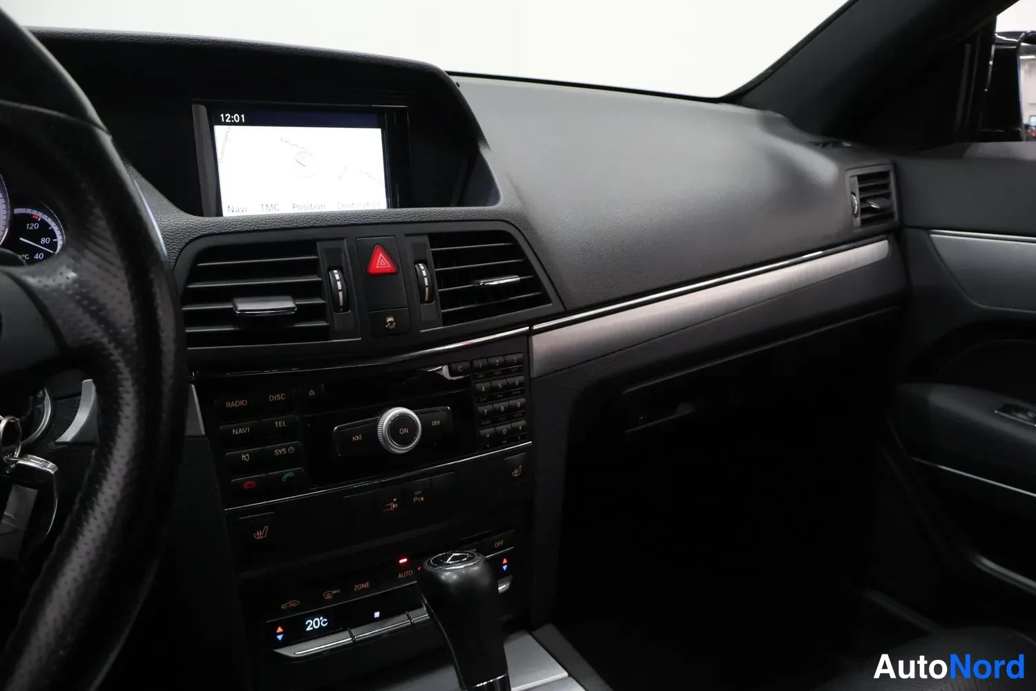 Muu: Mercedes-Benzin kojelauta ja keskikonsoli, jossa näytöllä karttanavigaatio, radio-napit ja automaattisen ilmastoinnin 20 °C -näyttö.
