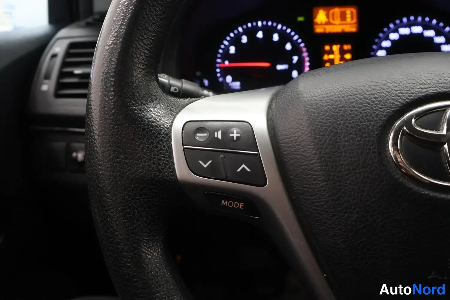 Muu: Rattiohjaimen äänensäädönpainikkeet (volyymi, MODE) ja Toyota-merkki, mittaristo taustalla.