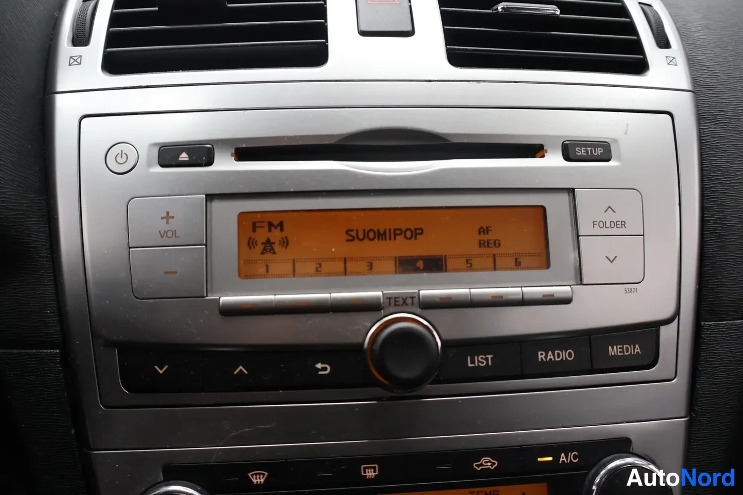 Yksityiskohta: Kojelaudan radioyksikkö, näytöllä teksti FM SUOMIPOP AF REG, oikealla SETUP- ja FOLDER-painikkeet.