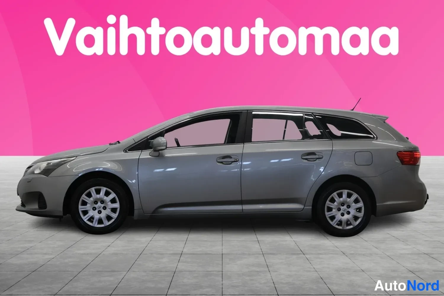 Etuviisto, nokka vasemmalle: Toyota Avensis Farmarikori, etuosa ja vasen sivu kolmasosa-kulmasta, hopeanharmaa.