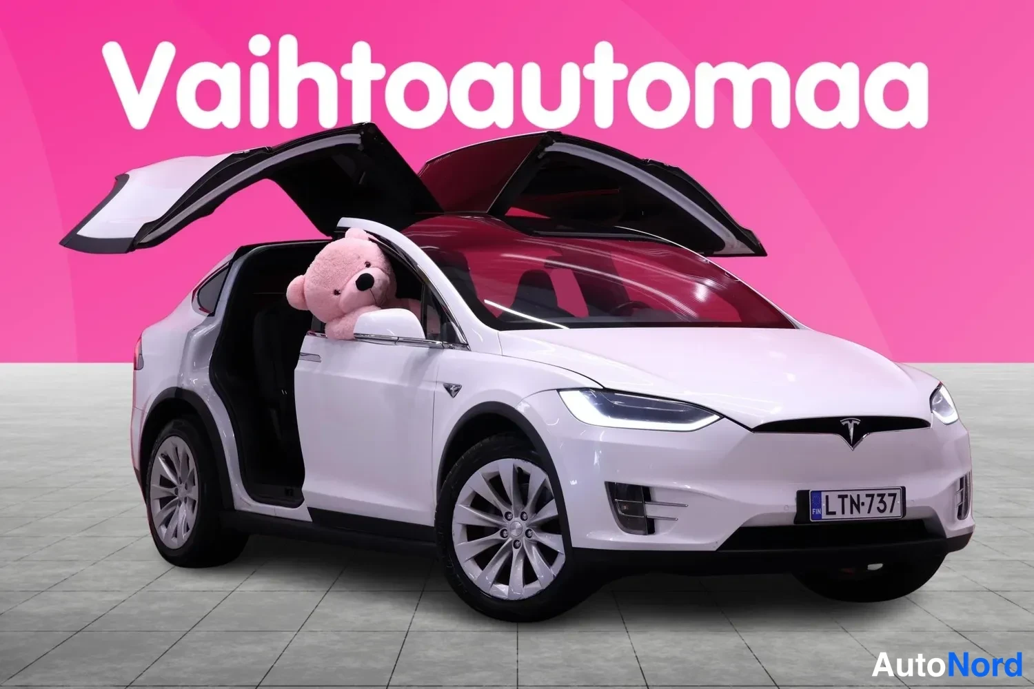 Etuviisto, nokka oikealle: Valkoinen Tesla Model X falcon wing -ovet auki, etuviisto oikealta.