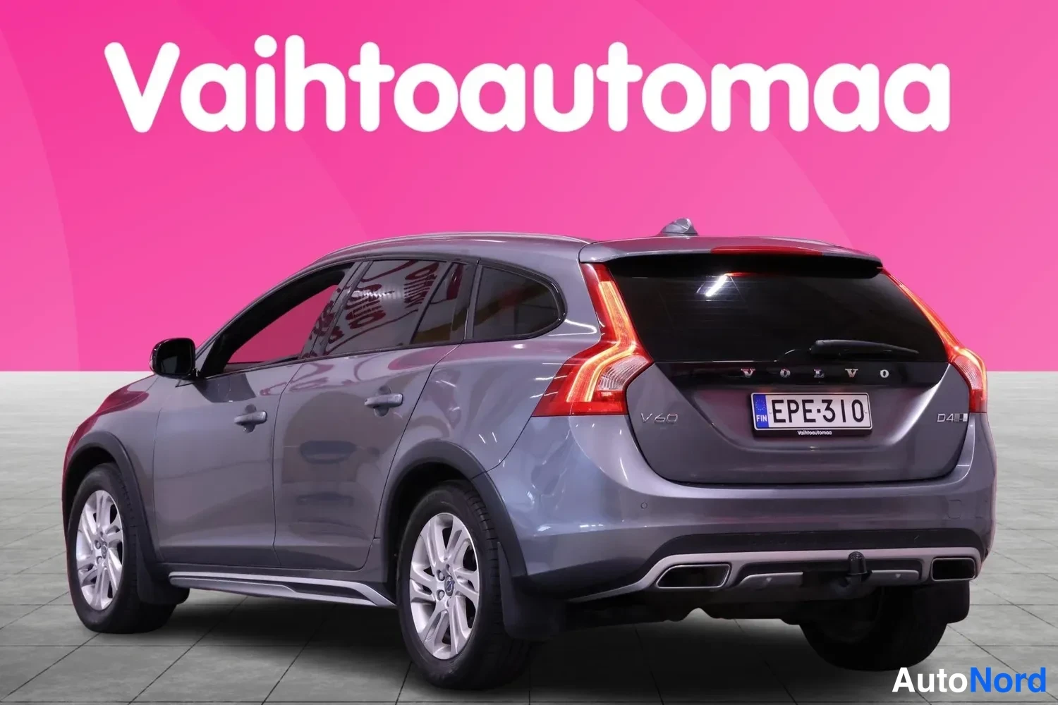Takaviisto: Rear three-quarter view of a grey station wagon with chrome trim, rear bumper lights and alloy wheels against pink background