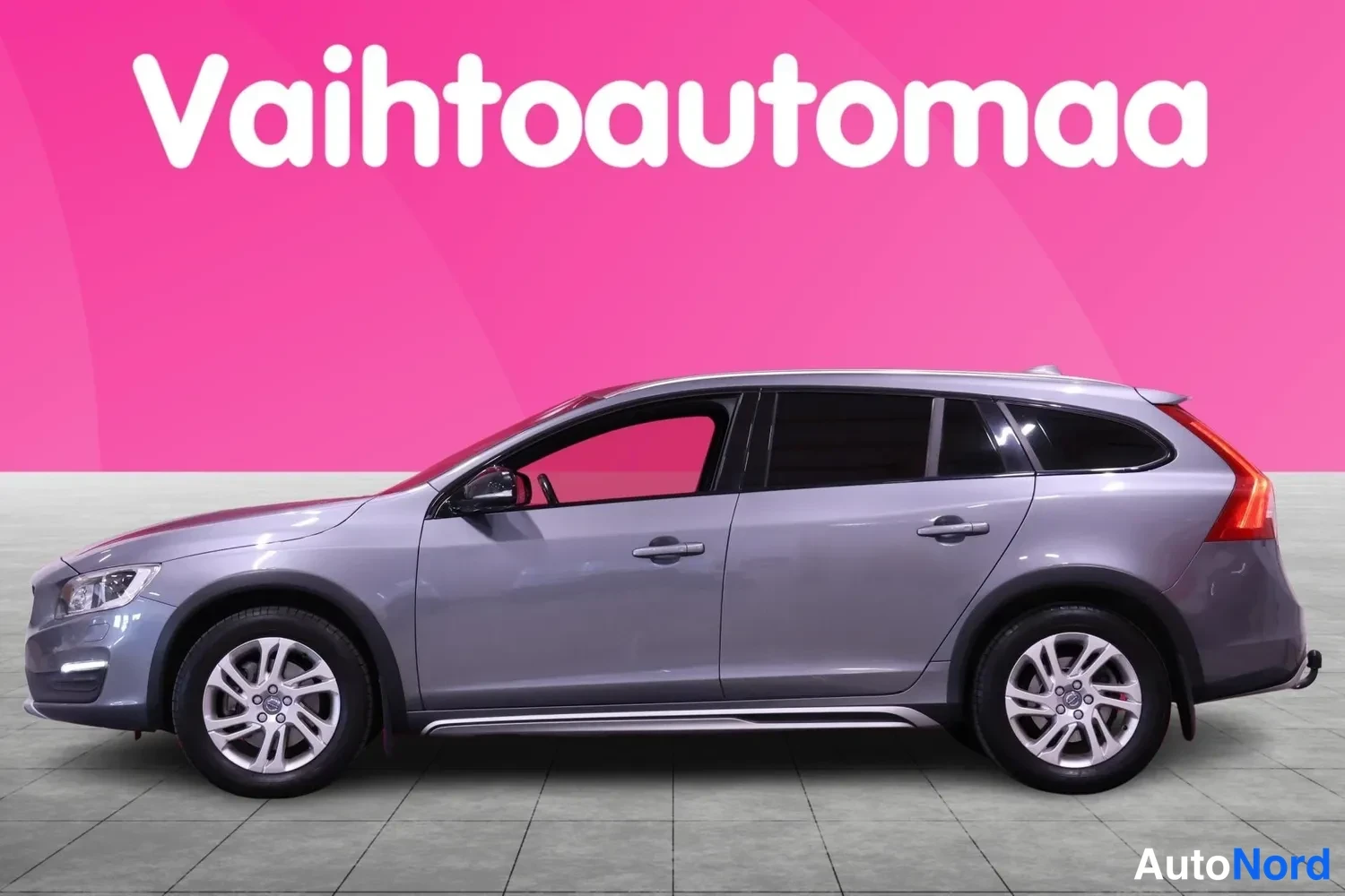Sivulta: Side profile shot of a grey station wagon with door handles, silver alloy wheels and side scuff plates against pink background