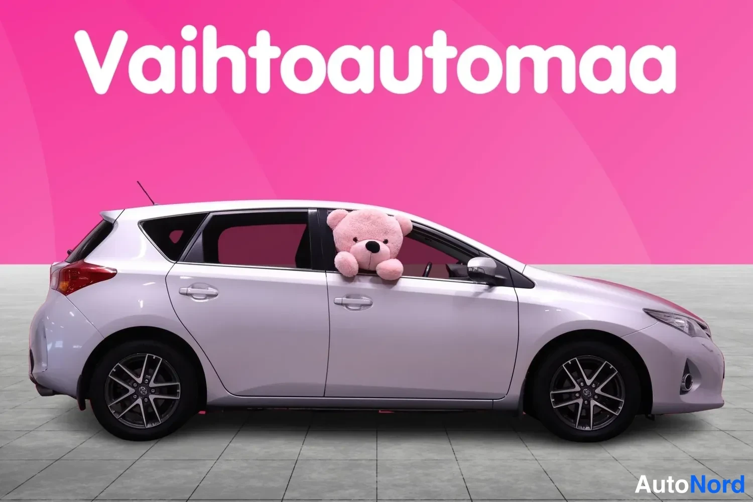 Sivulta: Sivu: Hopeanharmaa hatchback vasemmalta sivulta, jonka ovet ovat kiinni. Pehmolelu ikkunassa.