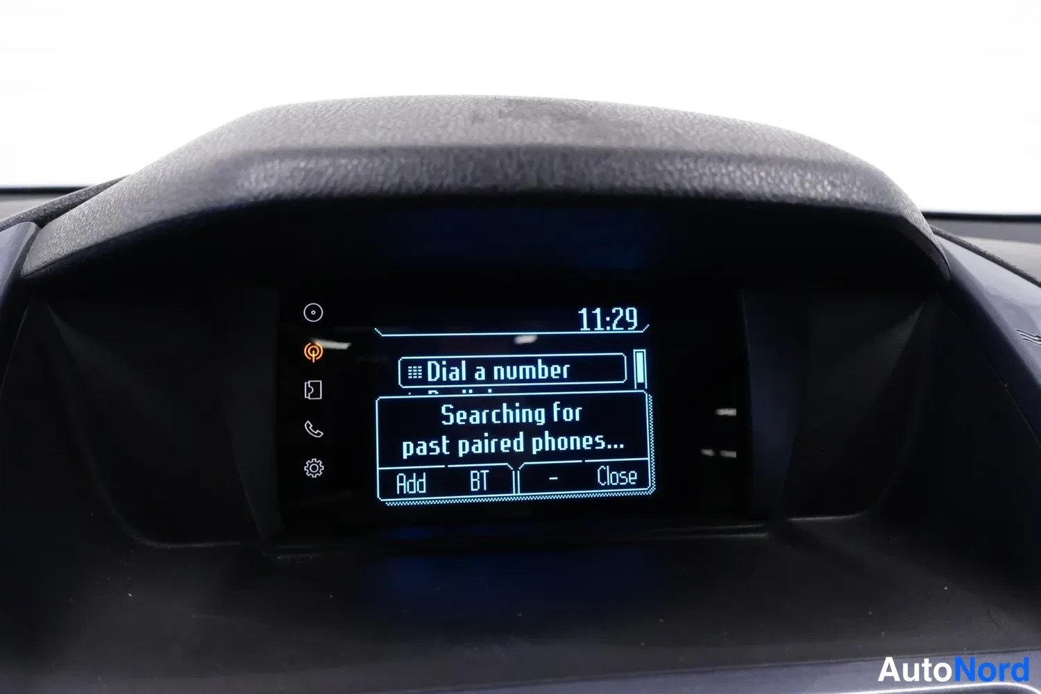 Muu: Kojelaudan näytön lähikuva: kello 11:29, valikossa Dial a number ja teksti Searching for past paired phones… sekä painikkeet Add, BT ja Close.