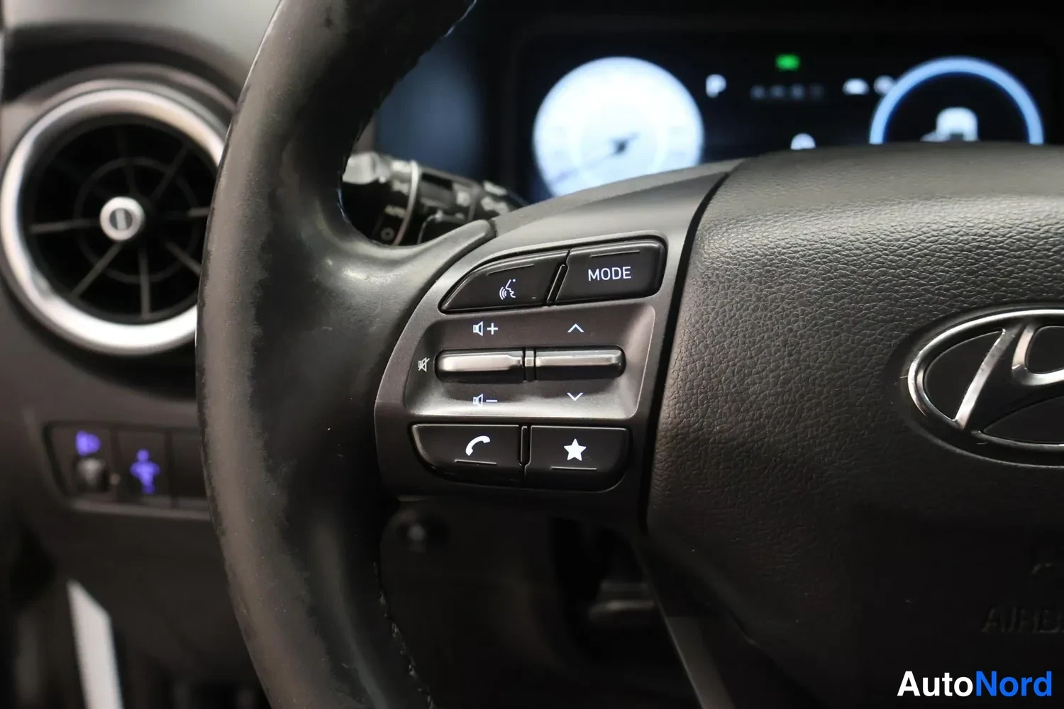 Muu: Ohjauspyörän vasemman puolen säädinpainikkeet lähikuvassa: MODE, äänen- ja puhelintoiminnot. Hyundai-logo ja kojelauta osittain näkyvissä.