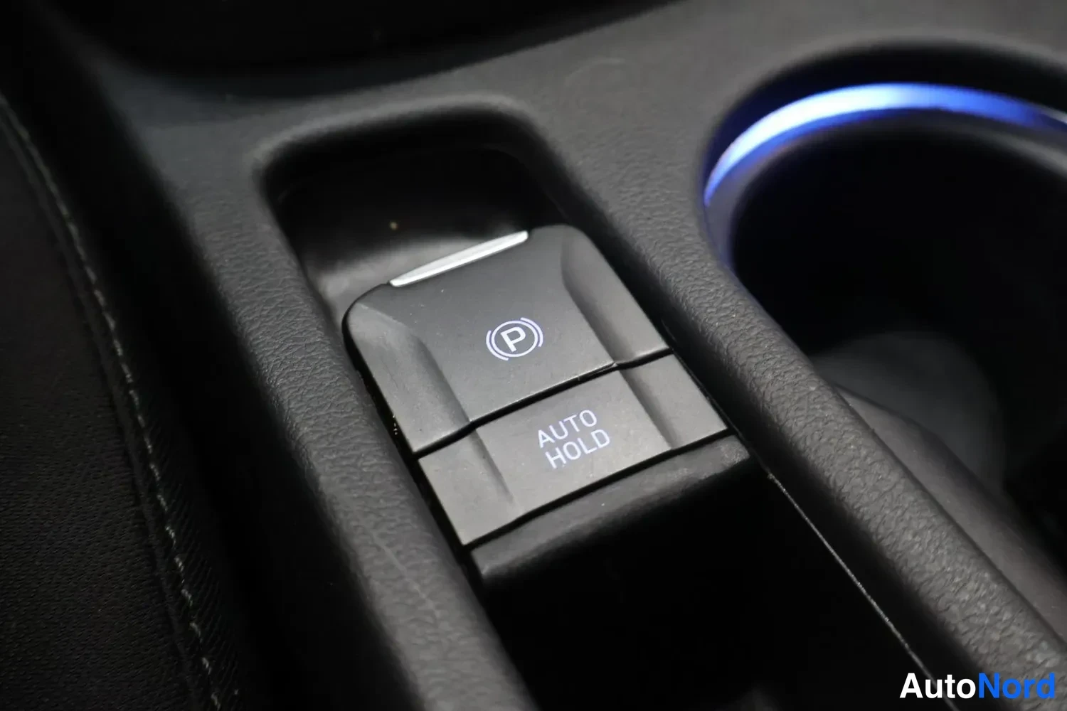 Yksityiskohta: Sähköinen peruutinpyyhkäisy? Ei — kuva sisätiloista: parkkitusti and AUTO HOLD -kytkimet keskikonsolissa.