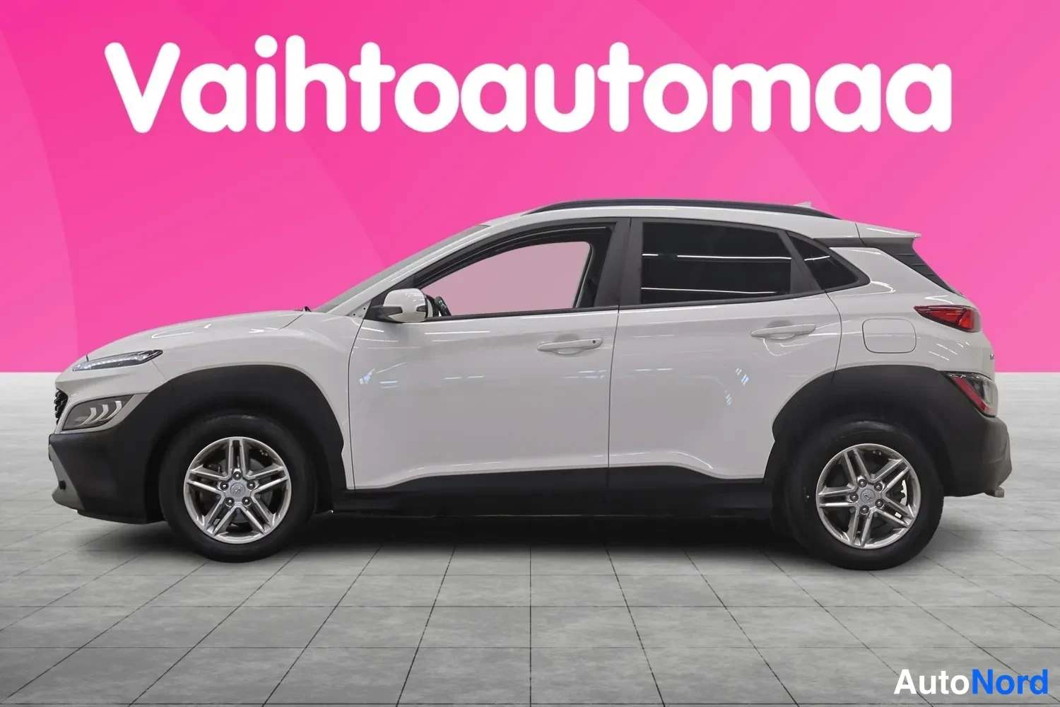 Etuviisto, nokka vasemmalle: Valkoisen Hyundai Kona -henkilöauton etukulma vasemmalta, koko auto näkyy vaaleassa studiossa.