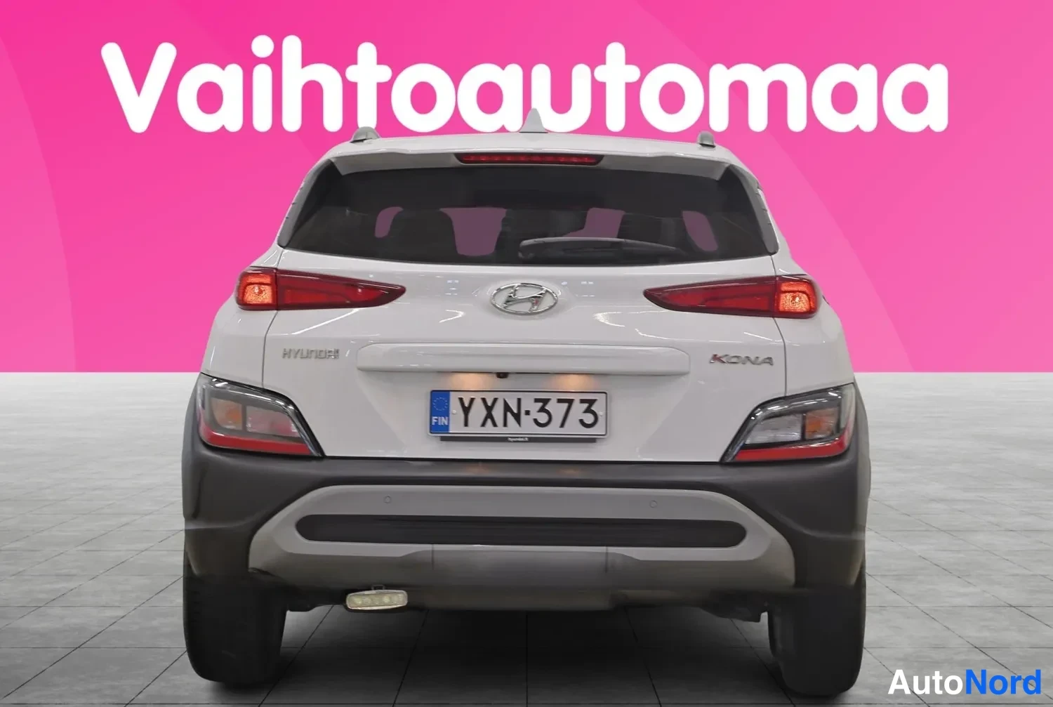 Takaa: Valkoisen Hyundai Kona -henkilöauton takaosa suoraan takaa, rekisterikilpi ja Kona-merkintä näkyvissä.