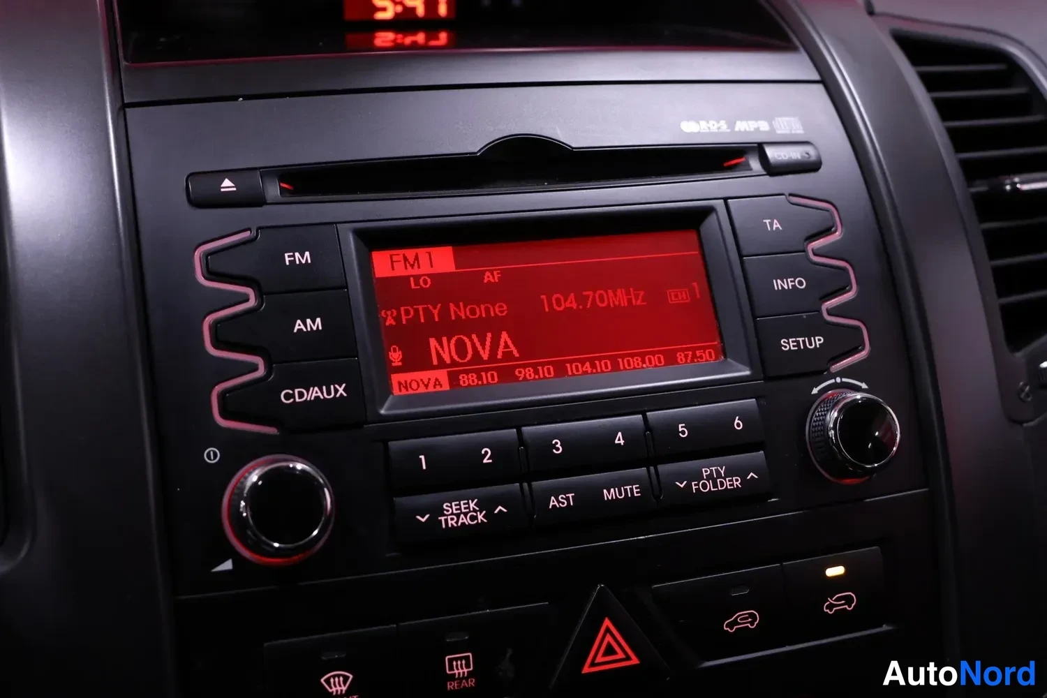 Yksityiskohta: Keskiössä radio-CD-yksikkö FM1-asteikolla 104.70 MHz (NOVA), näppäimet FM/AM/CD/AUX ja info/ta/setup.