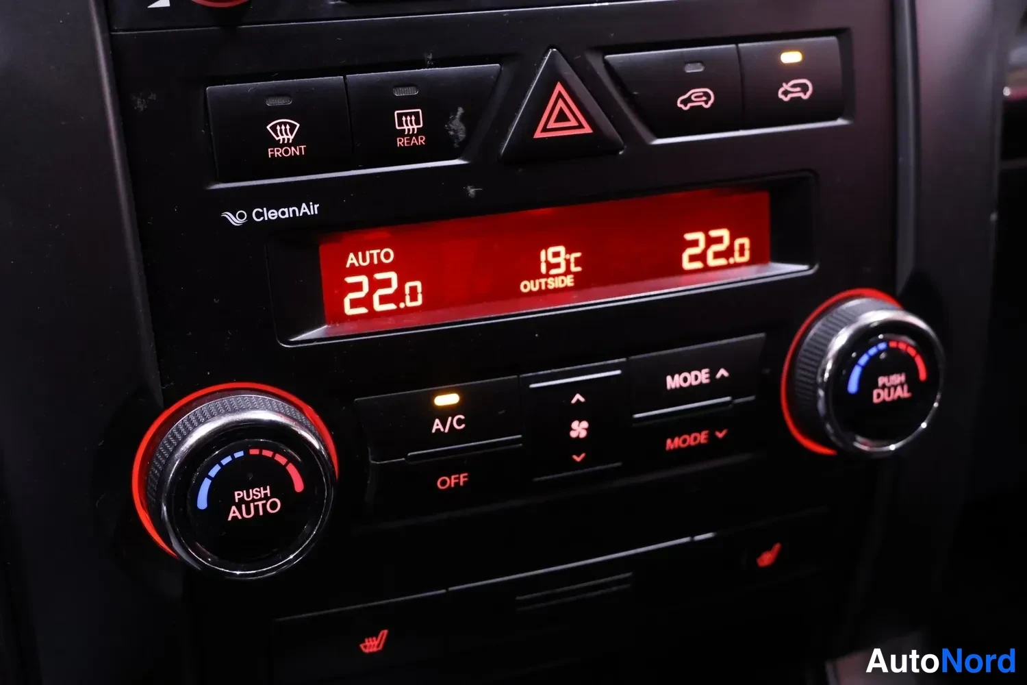 Muu: Automantt ilmastointipaneeli punaisella näytöllä: AUTO 22.0, ulkolämpötila 19°C, A/C-nappi ja PUSH AUTO/PUSH DUAL-säätönupit.