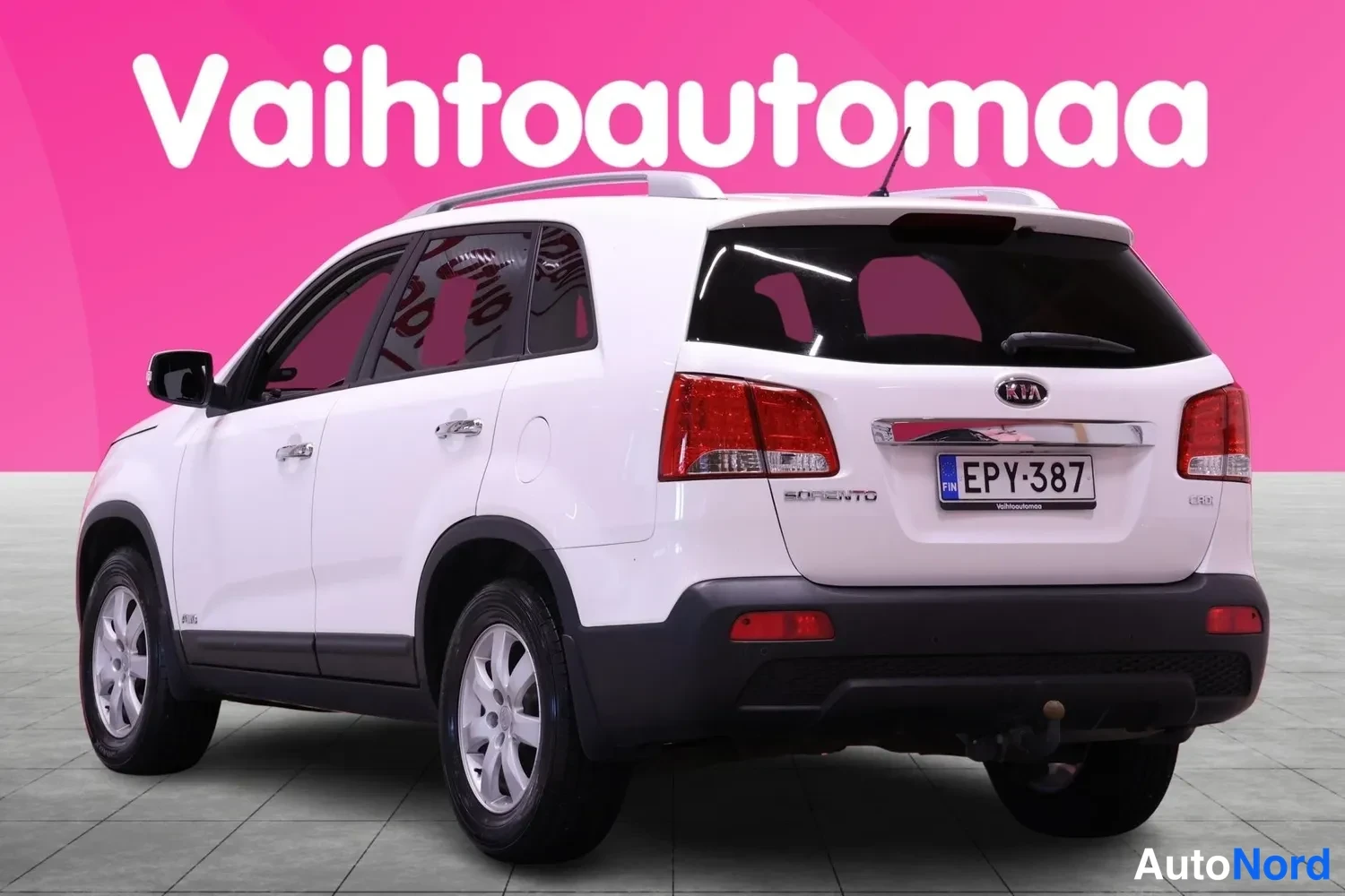 Takaviisto: Takasuurkulma valkoisesta Kia Sorentosta. Takavalot, tavaratilan kansi ja peräpalkki näkyvät. Kuvan oikeassa reunassa oleva takarenas on kauempana vasemmalla ku