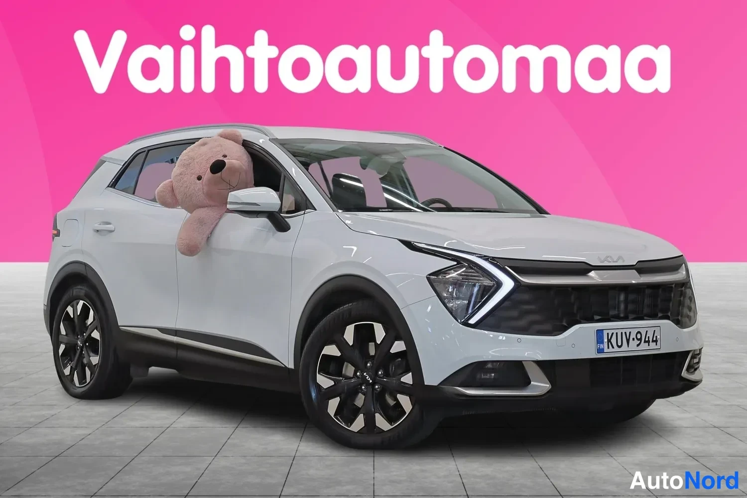 Etuviisto, nokka oikealle: Valkoinen Kia Sportage etukolmannesta näkymästä nokka oikealla; keulan etusäleikkö ja ajovalot sekä sivuovet ja takaosa näkyvät, rekisterikilpi.