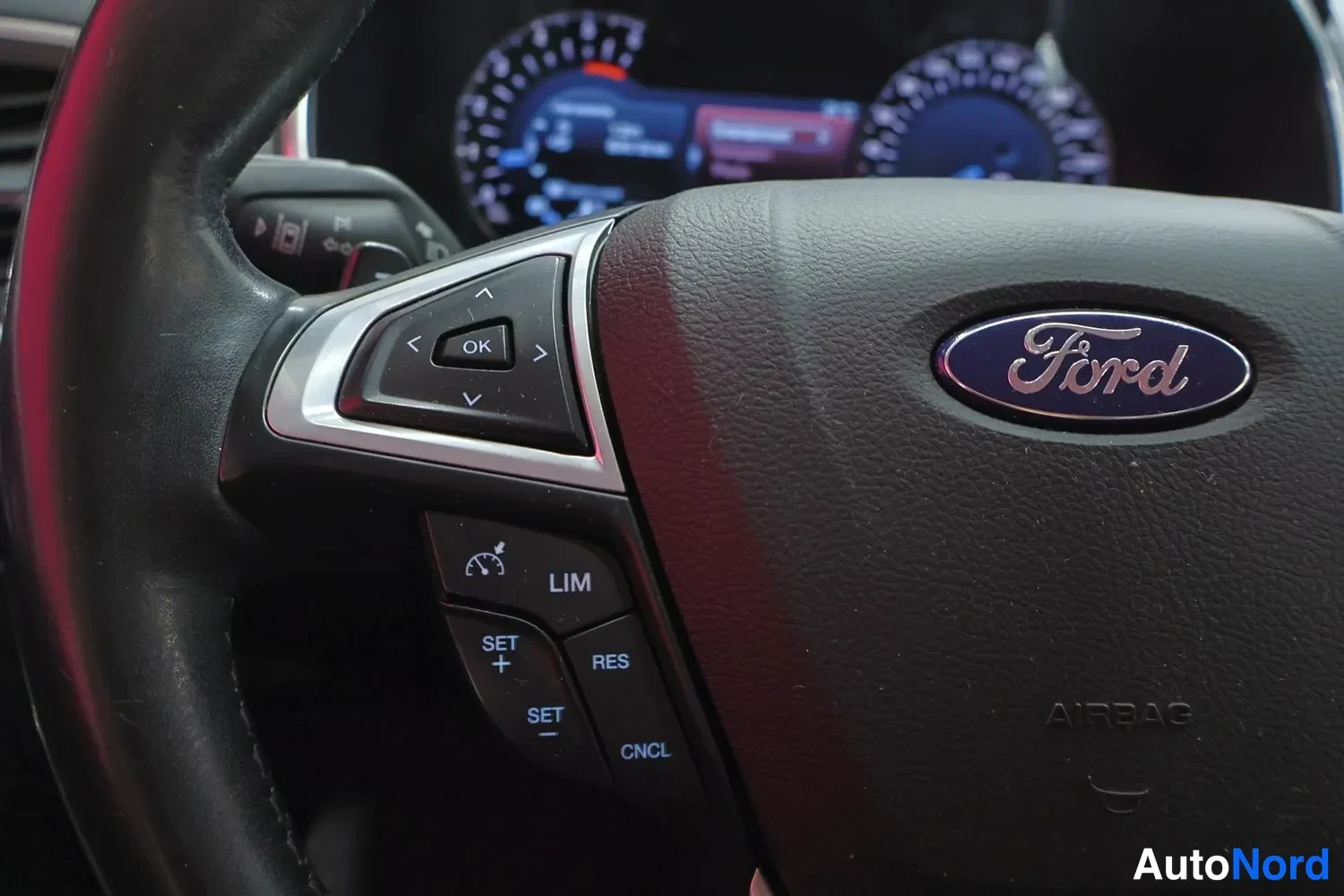 Yksityiskohta: Ford-ohjauspyörän lähikuva: AIRBAG-merkintä, nappien tekstit LIM, SET+, SET-, RES, CNCL ja OK.