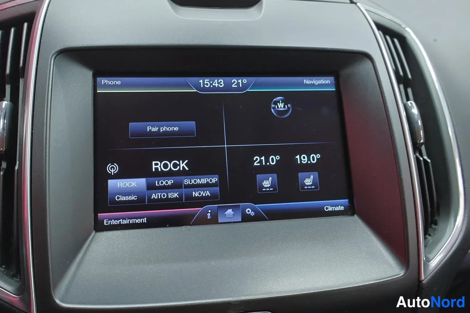 Yksityiskohta: Keskiöiston näyttö näyttää radiokanavalistaa (ROCK, SUOMIPOP, NOVA), lämpötilat 21,0° ja 19,0°, kellon 15:43 ja pariliitosvaihtoehdon Pair phone.