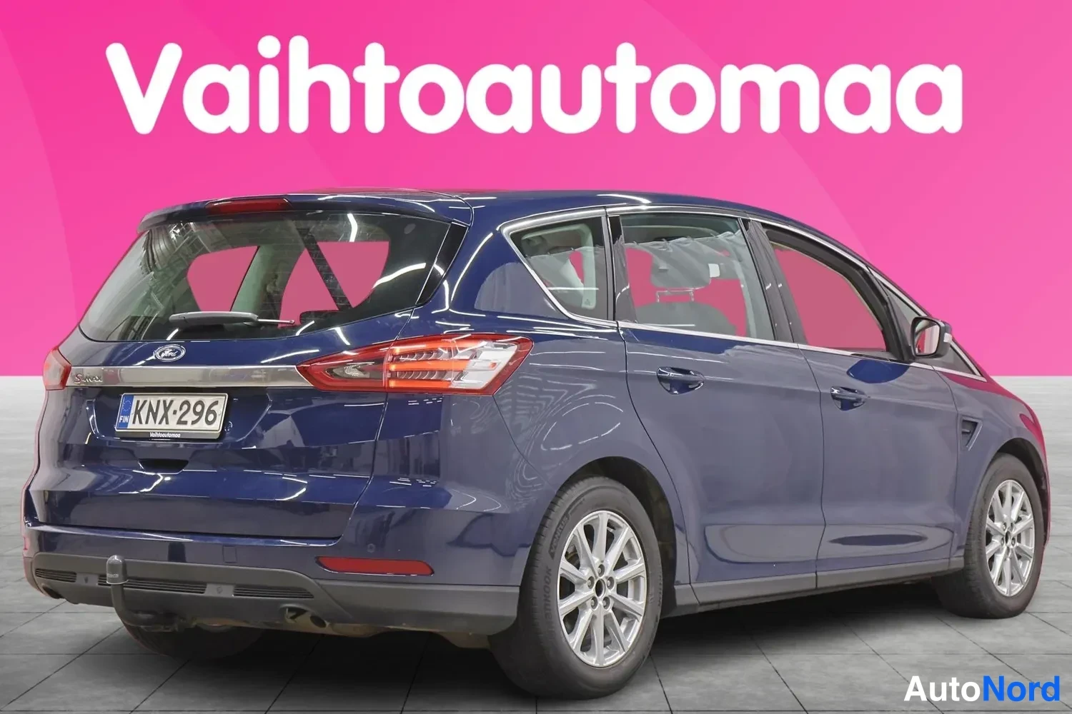 Takaviisto: Tummansininen Ford S-MAX takaa-vinosta toisesta kulmasta; rekisterikilpi ja vetokoukku näkyvissä.