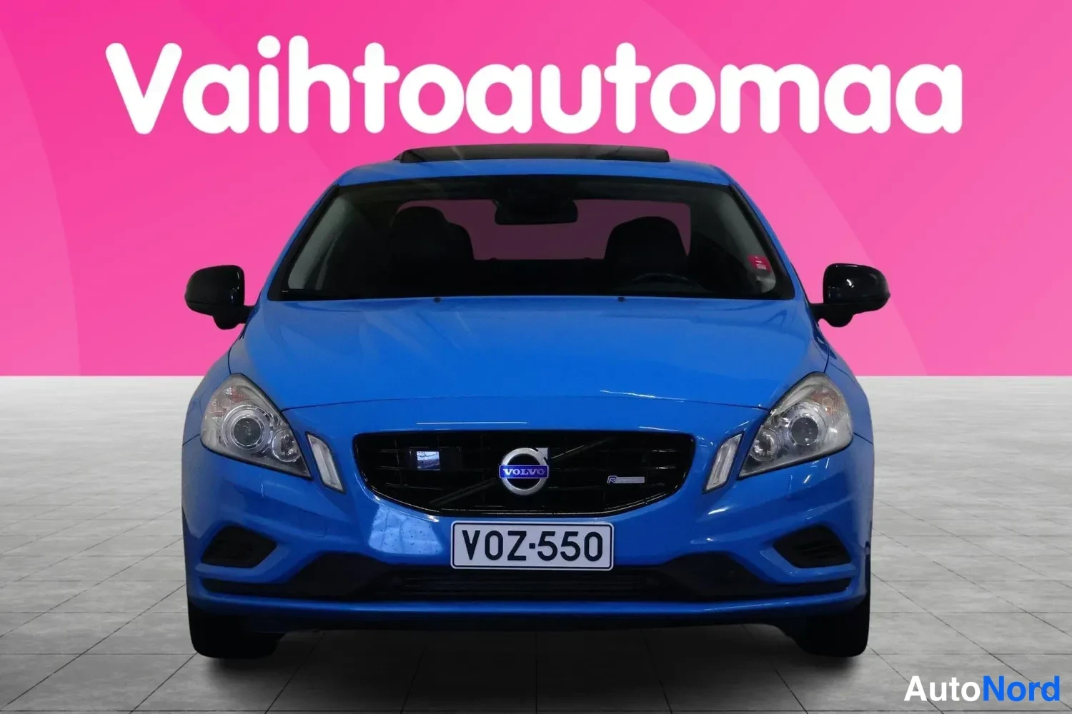 Edestä: Sininen Volvo S60 -henkilöauto suoraan edestä, rekisterikilpi.