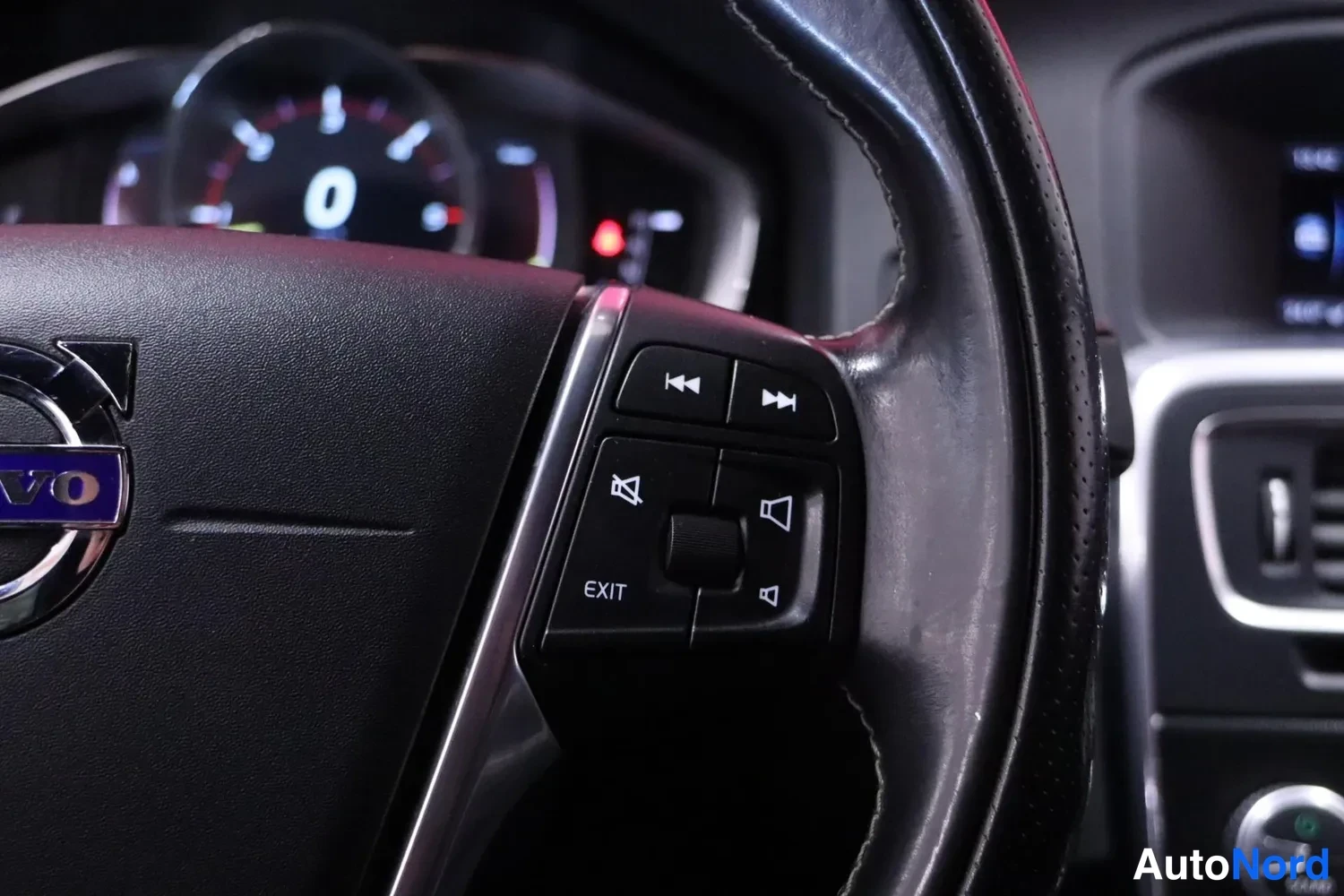 Muu: Ratin ohjainpainikkeet ja Volvo-emblem, taustalla mittaristo näyttää 0 km/h.