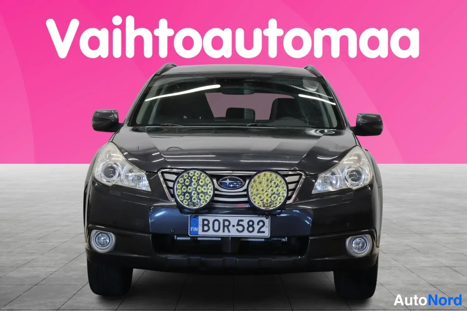Edestä: Tummanharmaa auto suoraan edestä, kylkykset ja takaosa eivät näy, rekisterikilpi.
