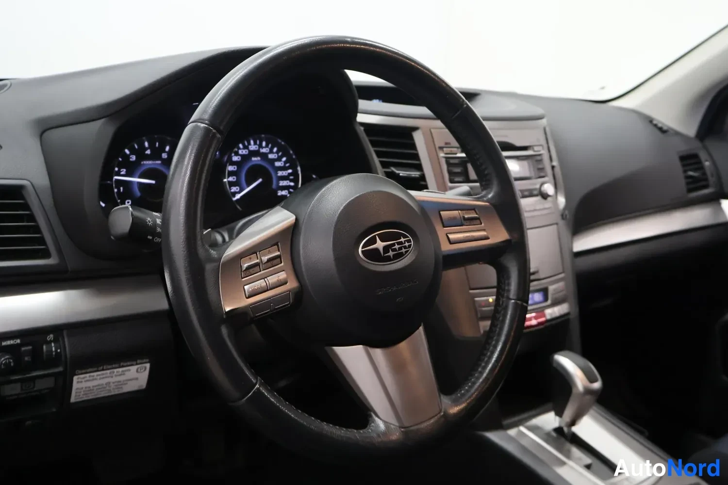 Muu: Ohjaamon näkymä: Subaru-merkkinen ohjauspyörä, takana mittaristo ja keskikonsolin äänentoistolaite.