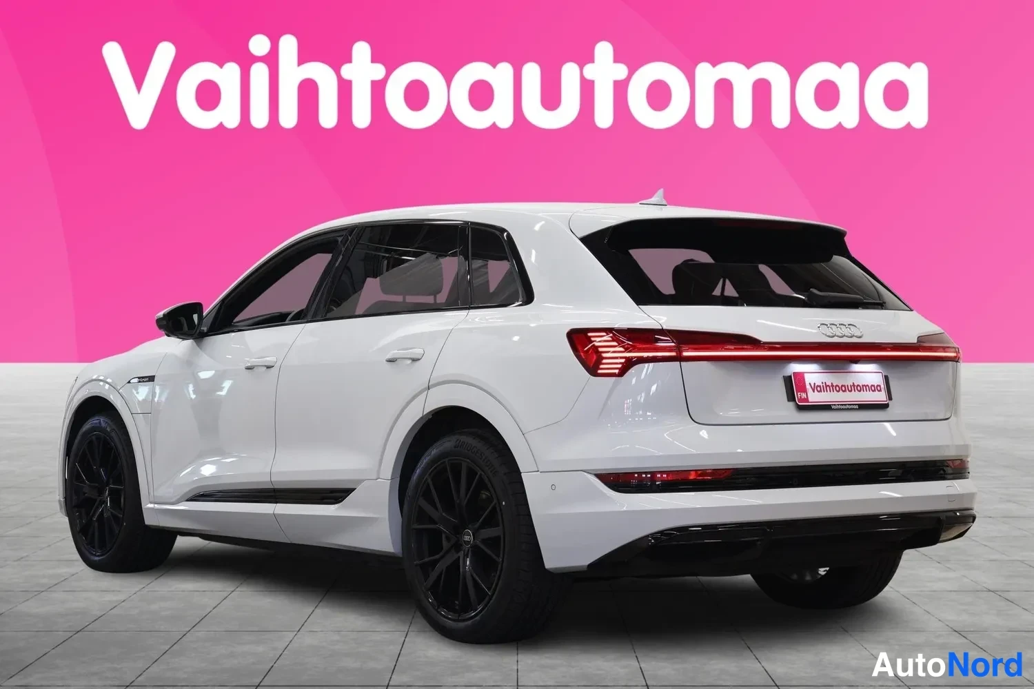 Takaviisto: Valkoinen Audi e-tron kolmestionurkkisesti takaa vasemmalta, pitkittäinen takavaloryhmä ja mustat vanteet