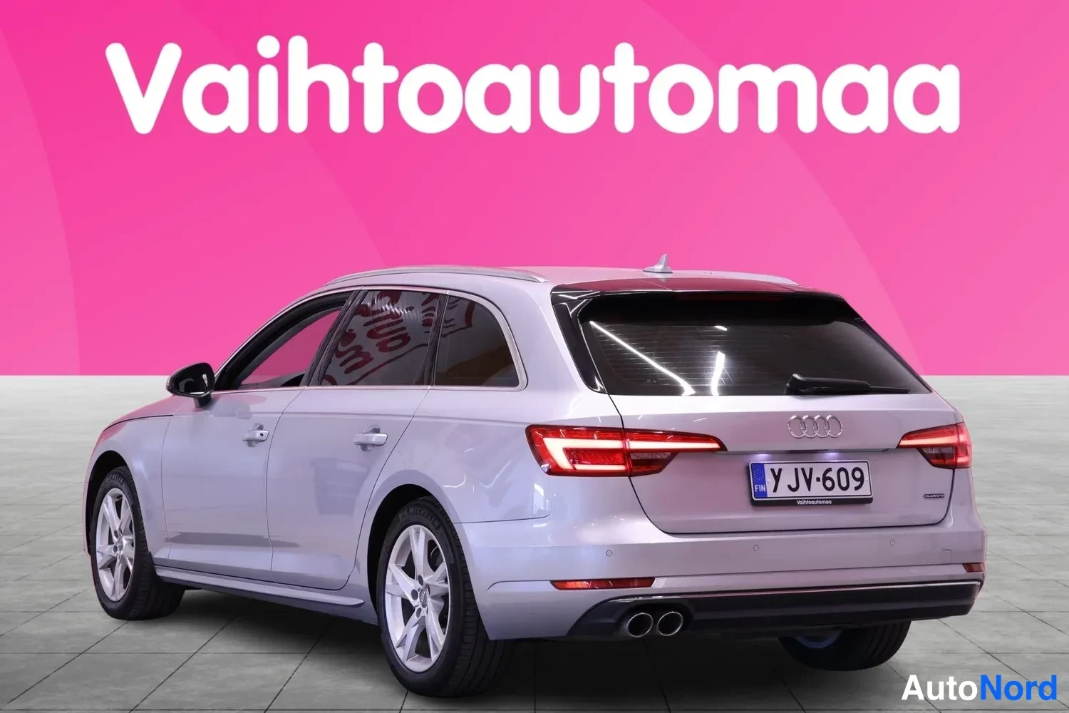 Takaviisto: Takapuolinen kolmionäkymä hopeisesta Audi-avannista. Takavalot, takaluukku, kaksoset puskurin putkit ja rekisterikilpi näkyvissä.