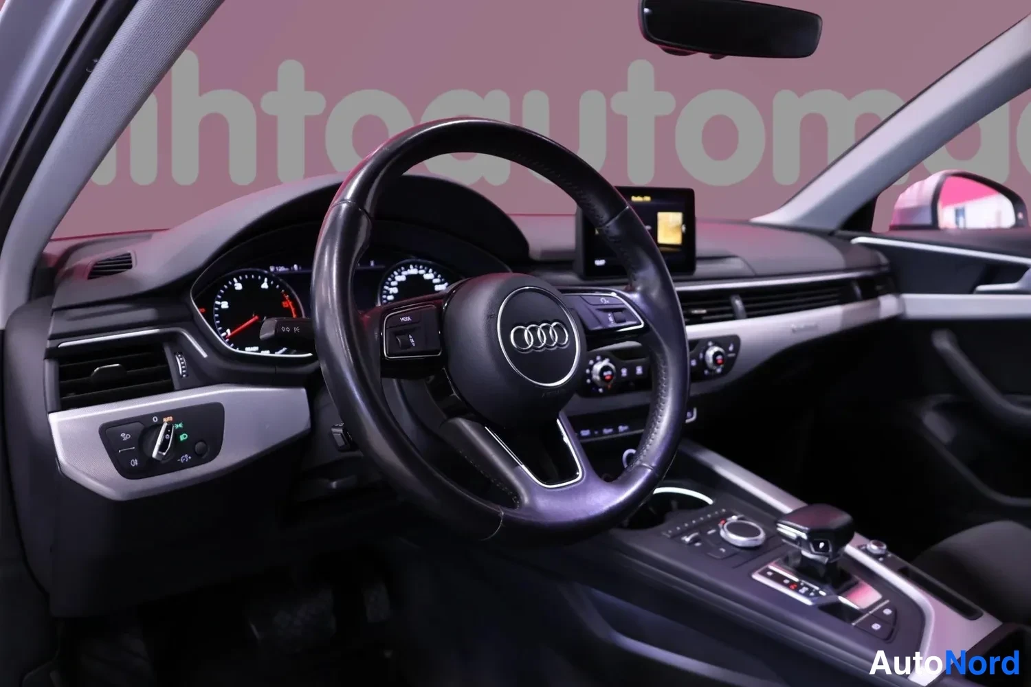 Edestä: Audi-ohjauspyörä, mittaristo ja keskikonsoli, tummat verhoilut.