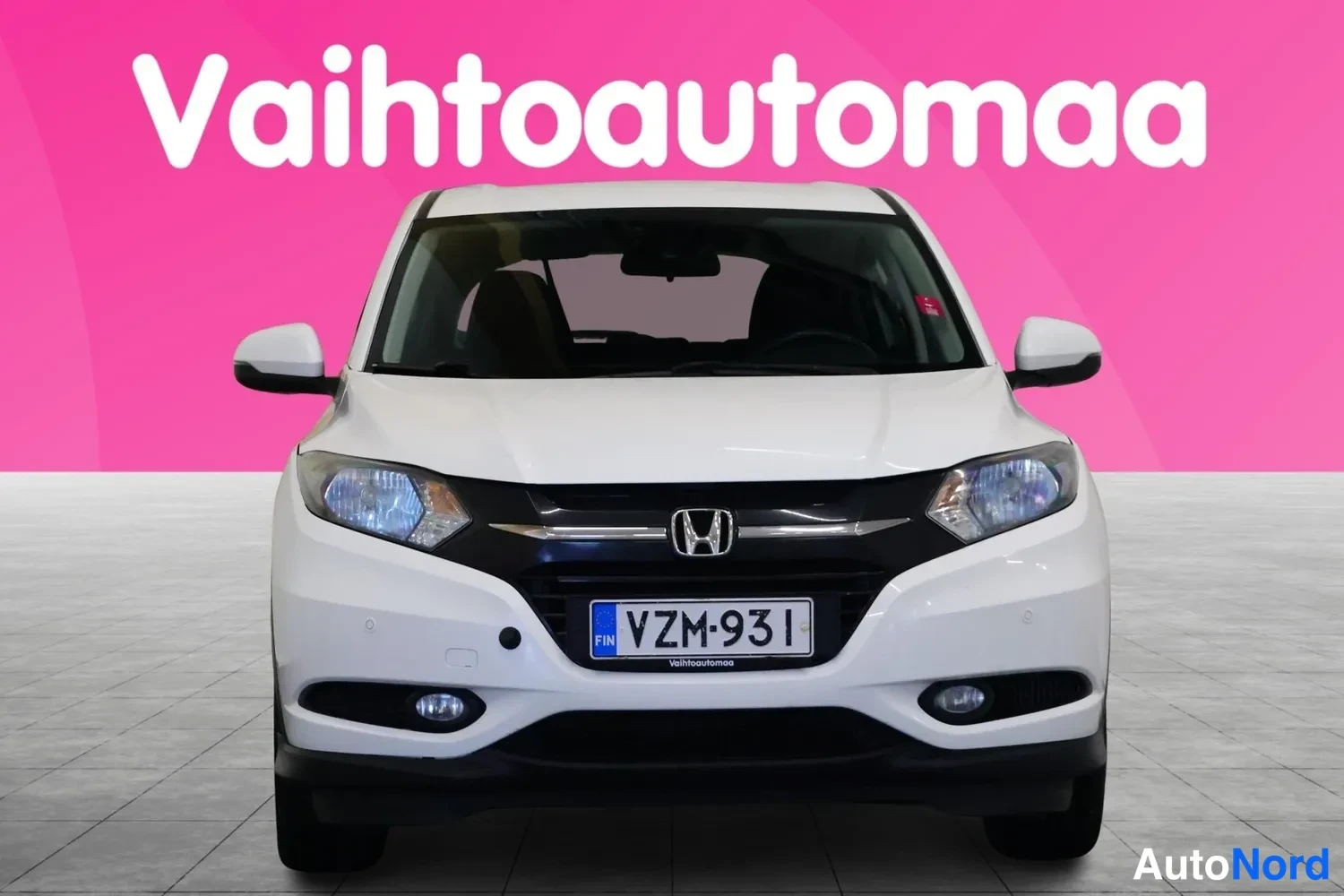 Edestä: Valkoisen Honda HR-V:n suora etunäkymä, rekisterikilpi, taustassa pinkki Vahtoautoma-mainoksen teksti.