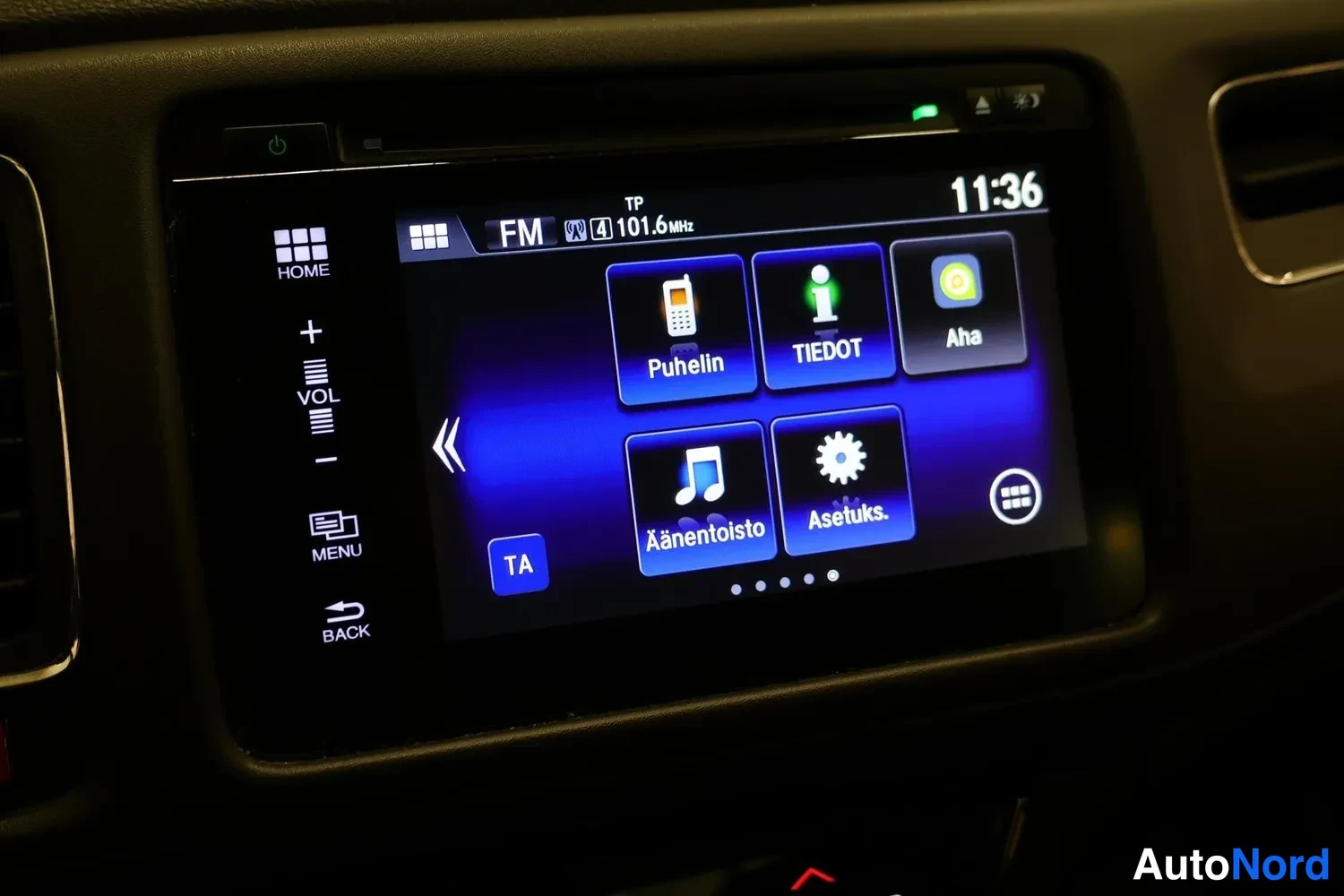 Yksityiskohta: Auton kosketusnäytön hallintapaneeli näyttää FM-radion taajuuden 101,6 MHz ja valikot Puhelin, TIEDOT, Aha, Ääentoisto ja Asetukset.