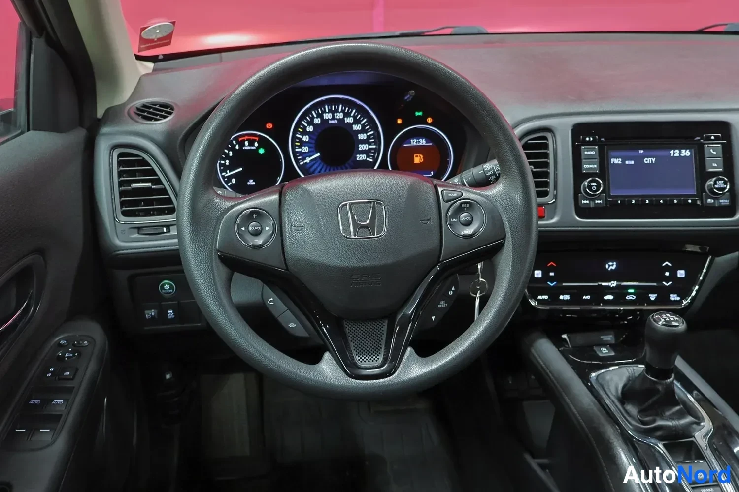 Edestä: Ohjaamo kokonaisuudessaan: Honda-merkkinen ohjauspyörä, analogiset mittarit, kosketusnäyttöradio ja manuaalivaihteiston vipu keskikonsolissa.