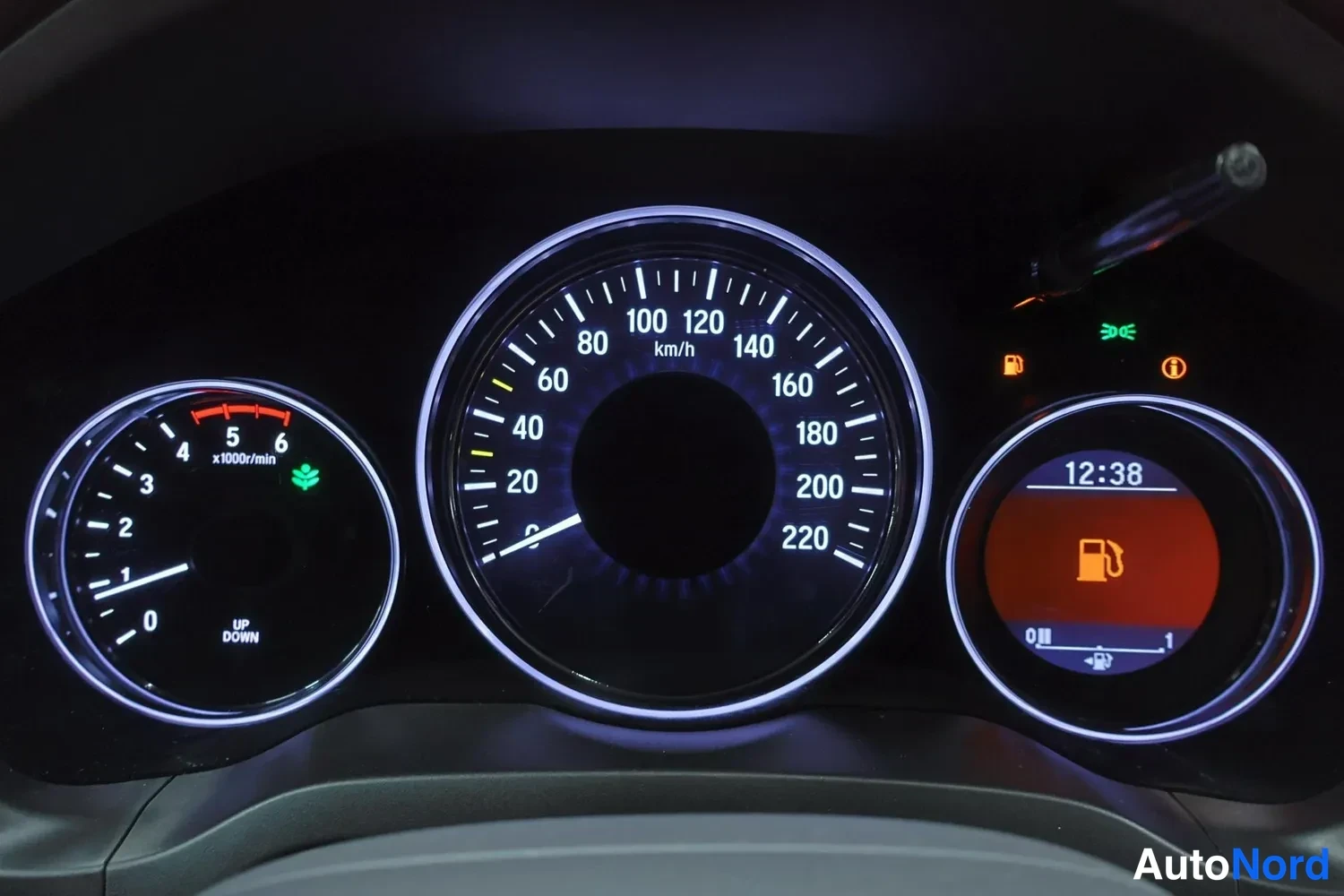 Edestä: Analoginen mittaristo suurennettuna: nopeusmittari 0–220 km/h, kierroslukumittari, kello (12:38) sekä polttoaine- ja eco-merkkivalot.
