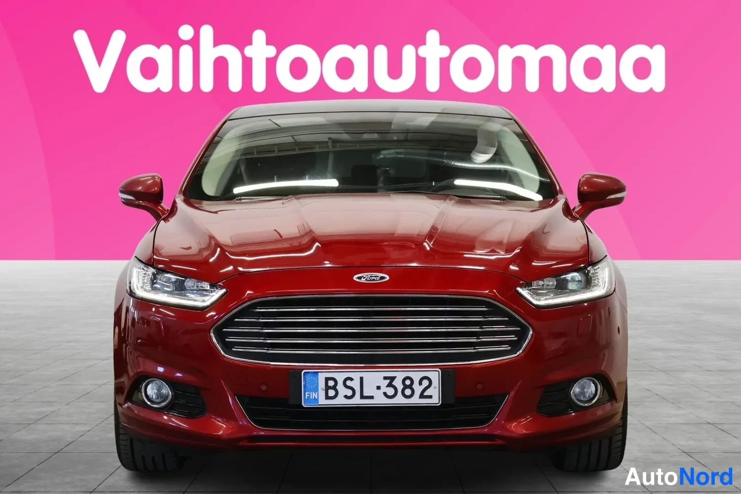 Edestä: Punainen Ford Mondeo -henkilöauto suoraan edestä, etusäleikkö ja ajovalot näkyvät; rekisterikilpi.
