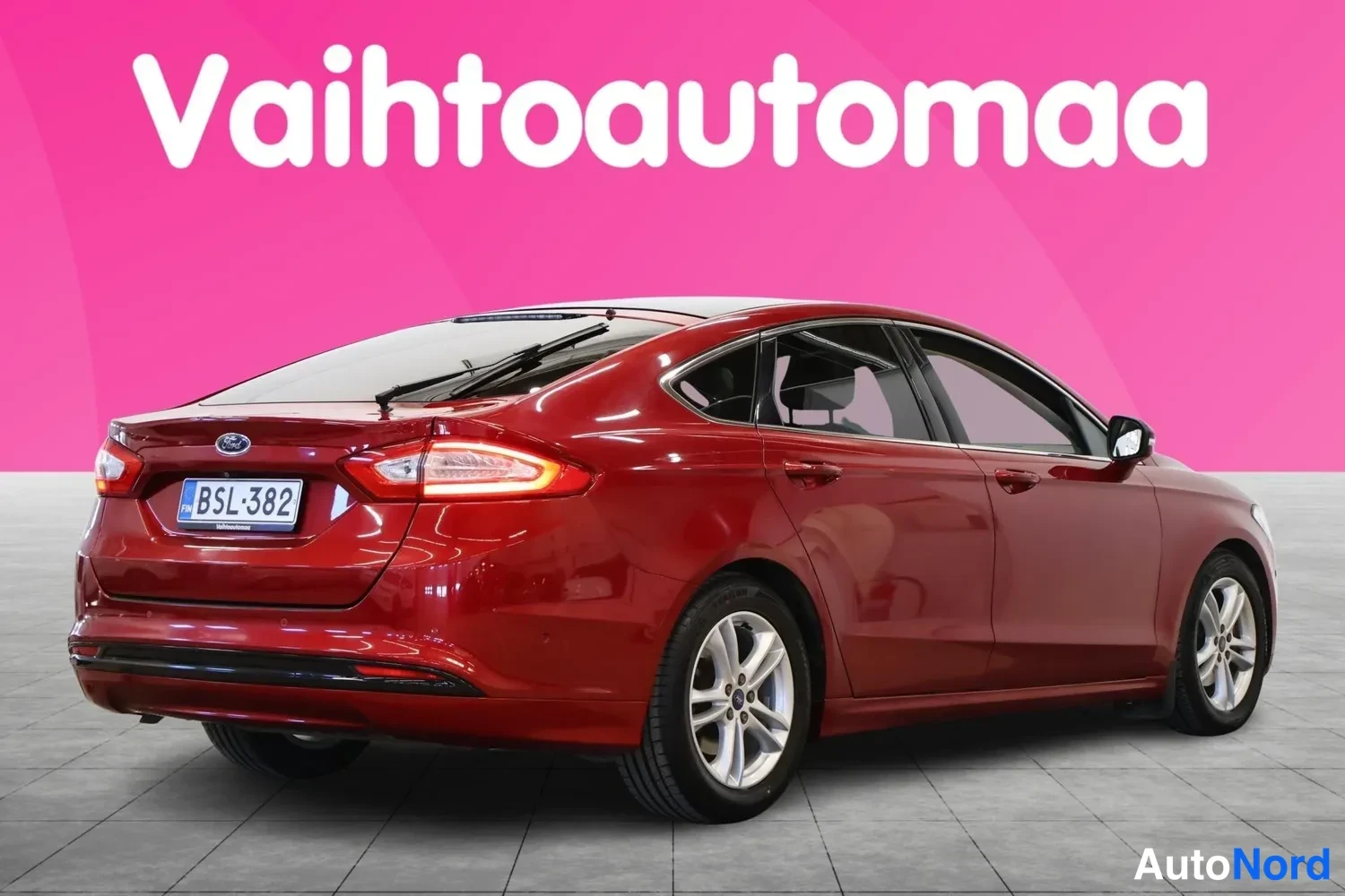 Takaviisto: Punainen Ford Mondeo oikealta takasivulta kuvattuna. Auto on valokuvattu studio-olosuhteissa kirkkaanpunaisen taustan edessä. Oikea puoli on näkyvissä mukaan lu