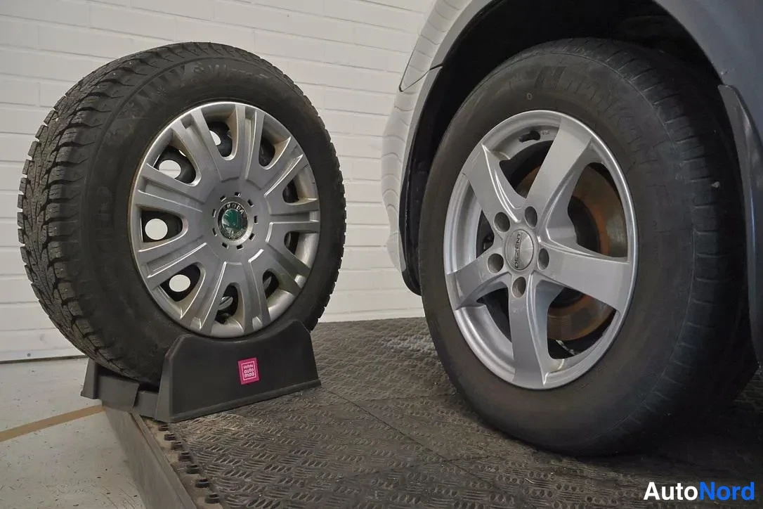 Yksityiskohta: Close-up shot showing two wheels on a metal ramp: a winter tyre on a multi-spoke alloy wheel standing on a stand next to a five-spoke alloy wheel mounted on the