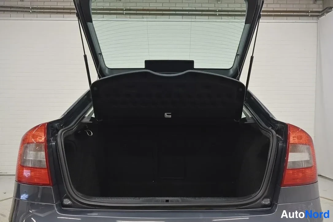 Tavaratila: Rear view of the car with the trunk open, showing the empty cargo area and the parcel shelf behind it. Tail lights and rear bumper are partially visible.