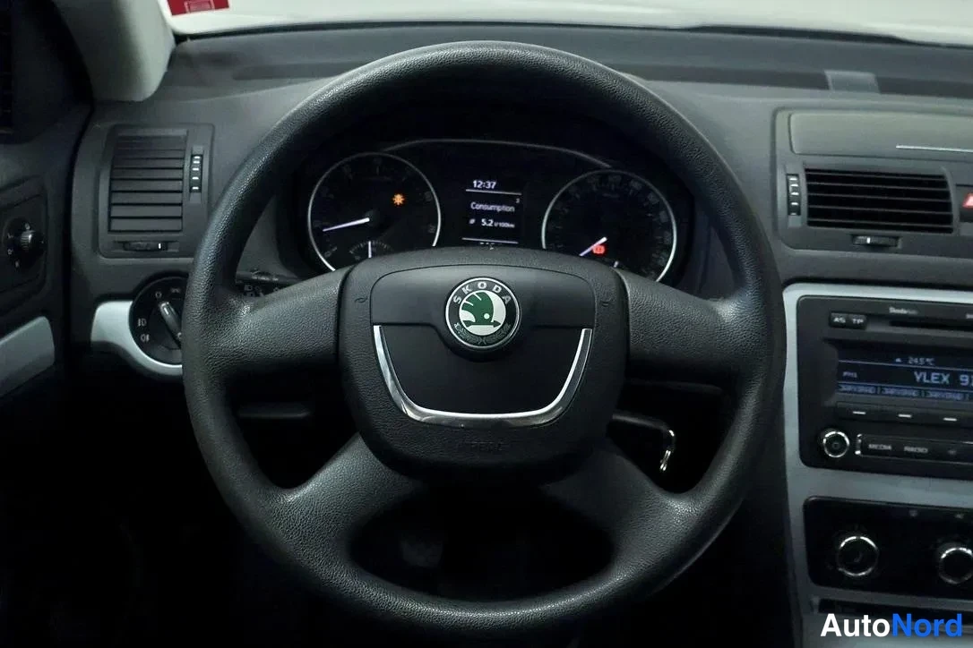 Yksityiskohta: Škoda-merkkinen ohjauspyörä, mittaristo näyttää kulutusta 5,2 l/100 km, kojelaudan radiopaneeli näkyy oikealla.
