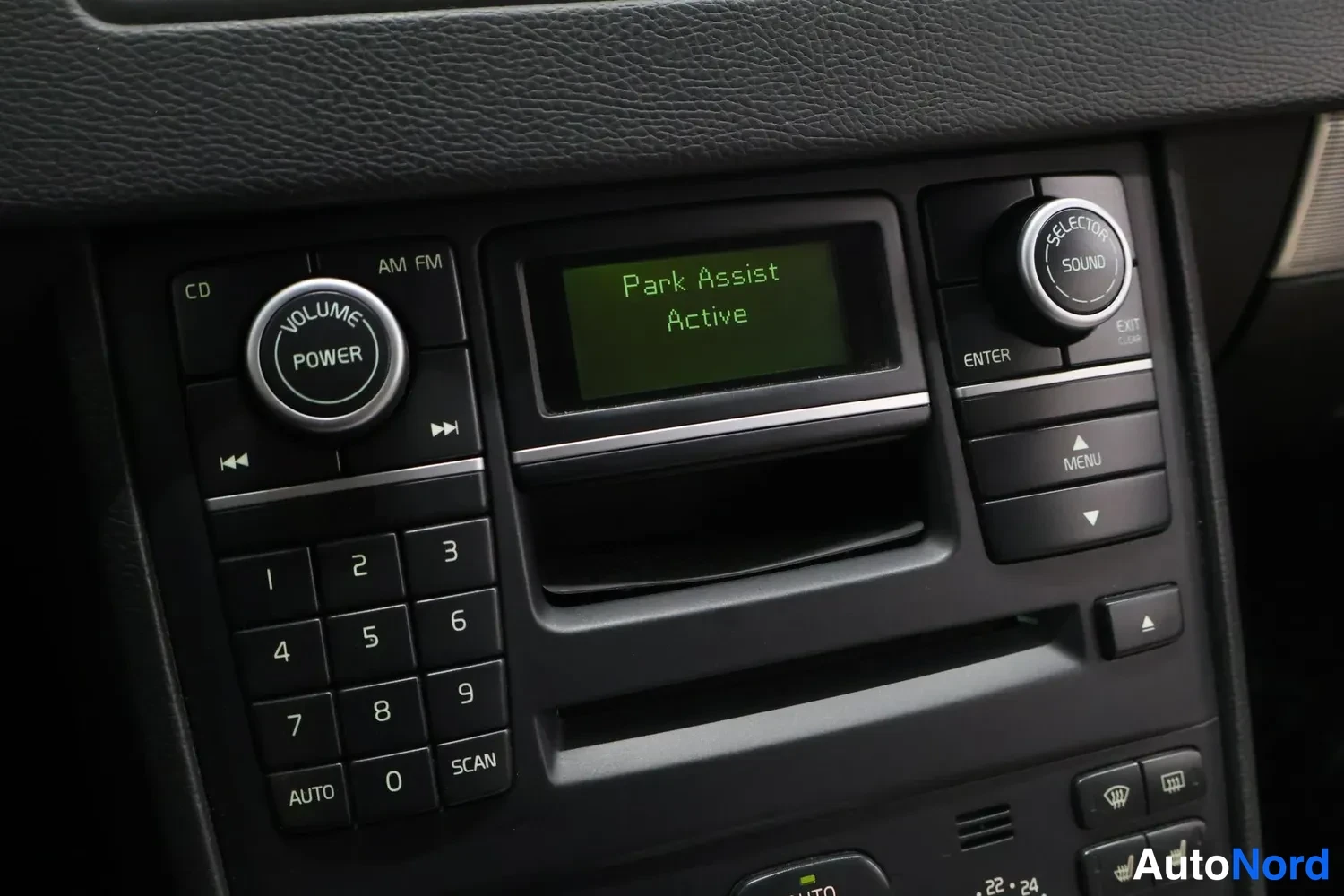 Muu: Keskikonsolin radiopaneeli: VOLUME POWER -nuppi, CD/AM FM -merkit, numeronäppäimet ja näytössä teksti Park Assist Active.