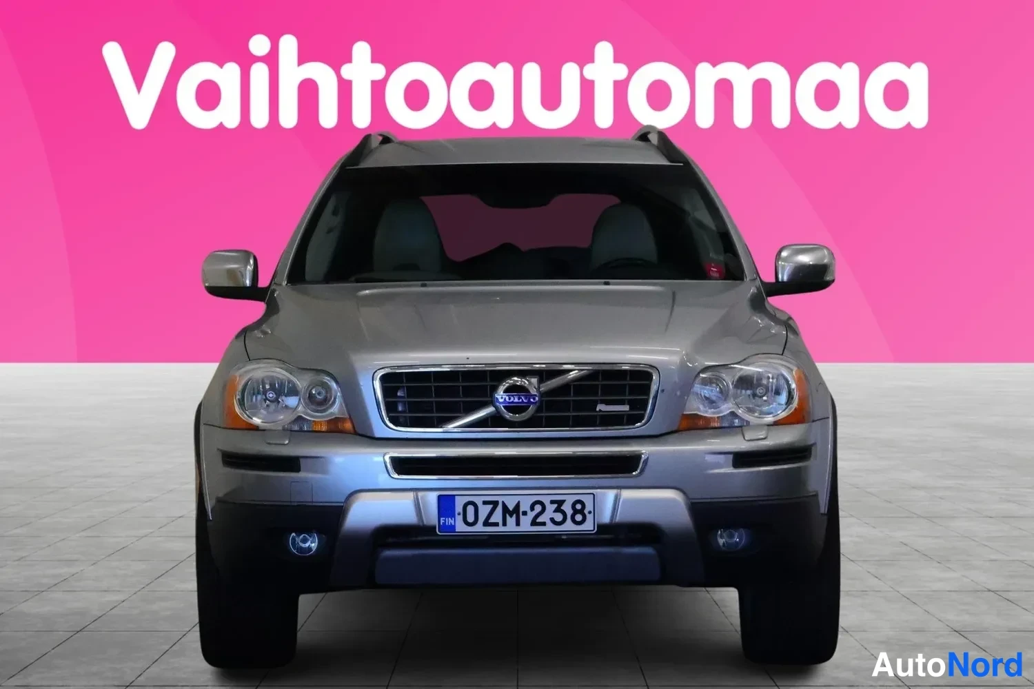 Edestä: Hopeanharmaa Volvo XC90 suoraan edestäpäin, rekisteritunnus, Volvo-merkki jäähdyttijän säleikössä.