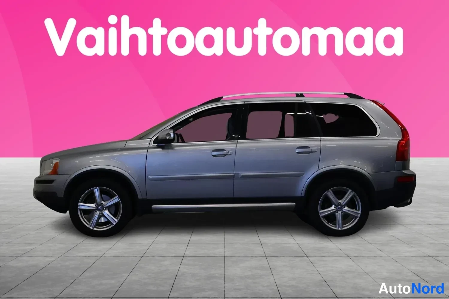 Sivulta: Hopeanharmaa Volvo XC90 sivusta oikealta puolelta, kattokisko ja hopeiset vanteet näkyvissä.