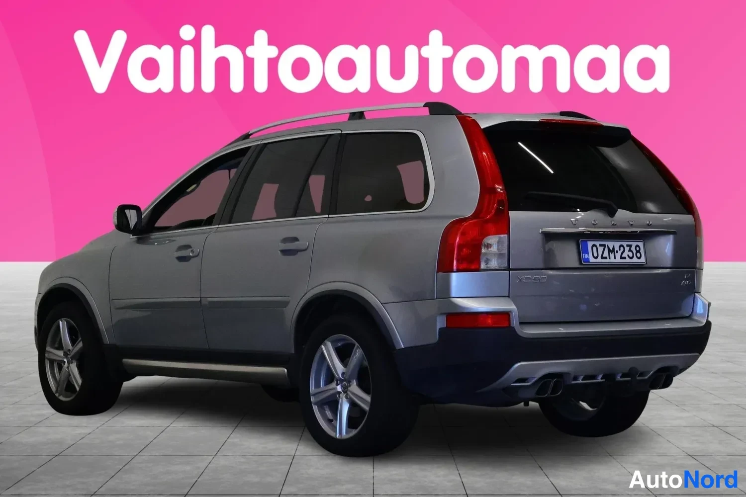 Takaviisto: Hopeanharmaa Volvo XC90 takakulmasta vasemmalta, rekisteritunnus, takavalo ja kattokisko näkyvissä.