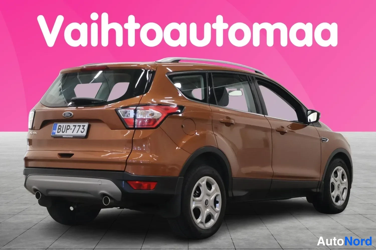 Takaviisto: Ruskea Ford Kuga kuvattu takakulmasta vasemmalta, rekisterikilpi, kaksi pakoputkea ja hopeiset kevytmetallivanteet näkyvät.